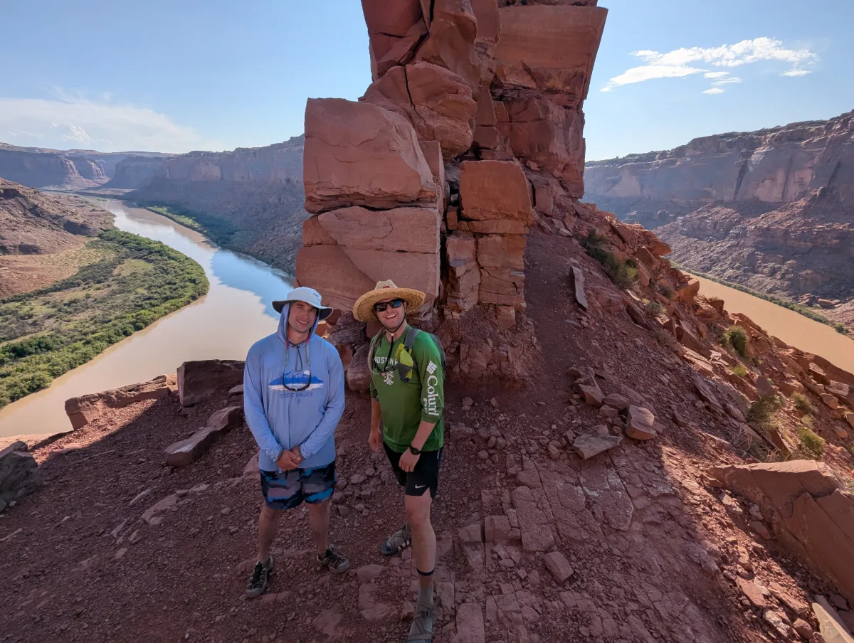Logan and a friend in sun hats on a red-rock ridge high above the Green River's horseshoe bend.